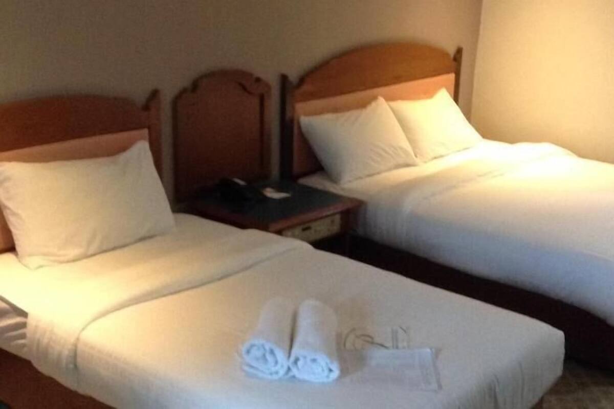 Habitación de hotel con dos camas individuales, una mesita de noche y un par de toallas sobre la cama.