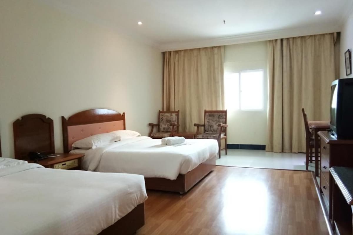A hotel room with two beds, a television, and a desk.