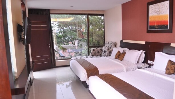 Quarto de hotel com duas camas, uma janela grande com vista para árvores e um quadro na parede.