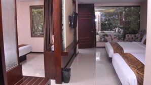 Quarto de hotel com cama, sofá, televisão e porta de vidro deslizante para uma varanda.