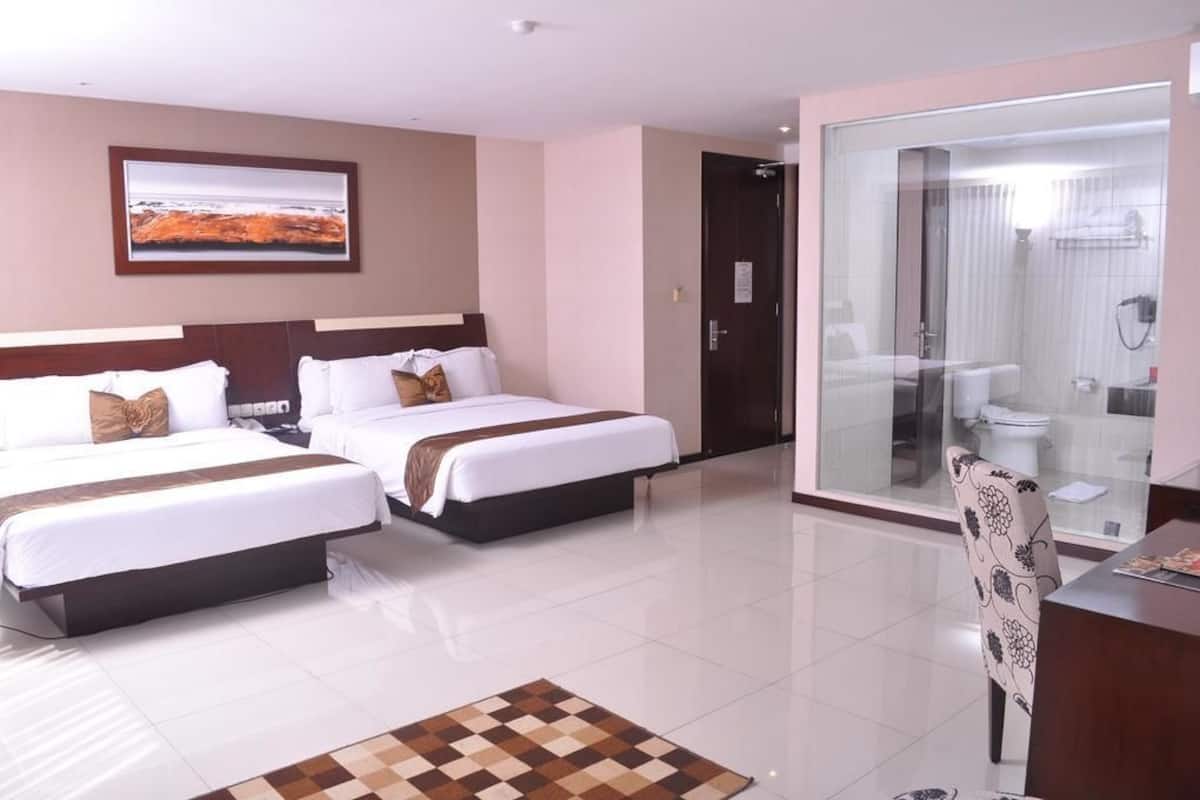 A hotel room with two beds, a desk, a chair, a glass shower enclosure, and a framed picture on the wall.