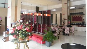 Um hall amplo com um sofá vermelho, uma mesa de vidro com um arranjo floral e uma área de recepção com cortina vermelha.