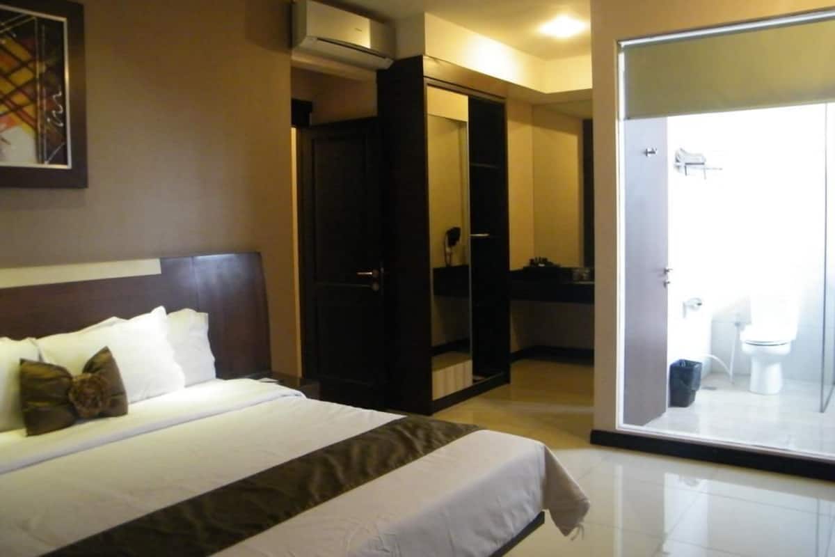 A hotel room with a bed, a wardrobe, and a bathroom visible through a glass door.