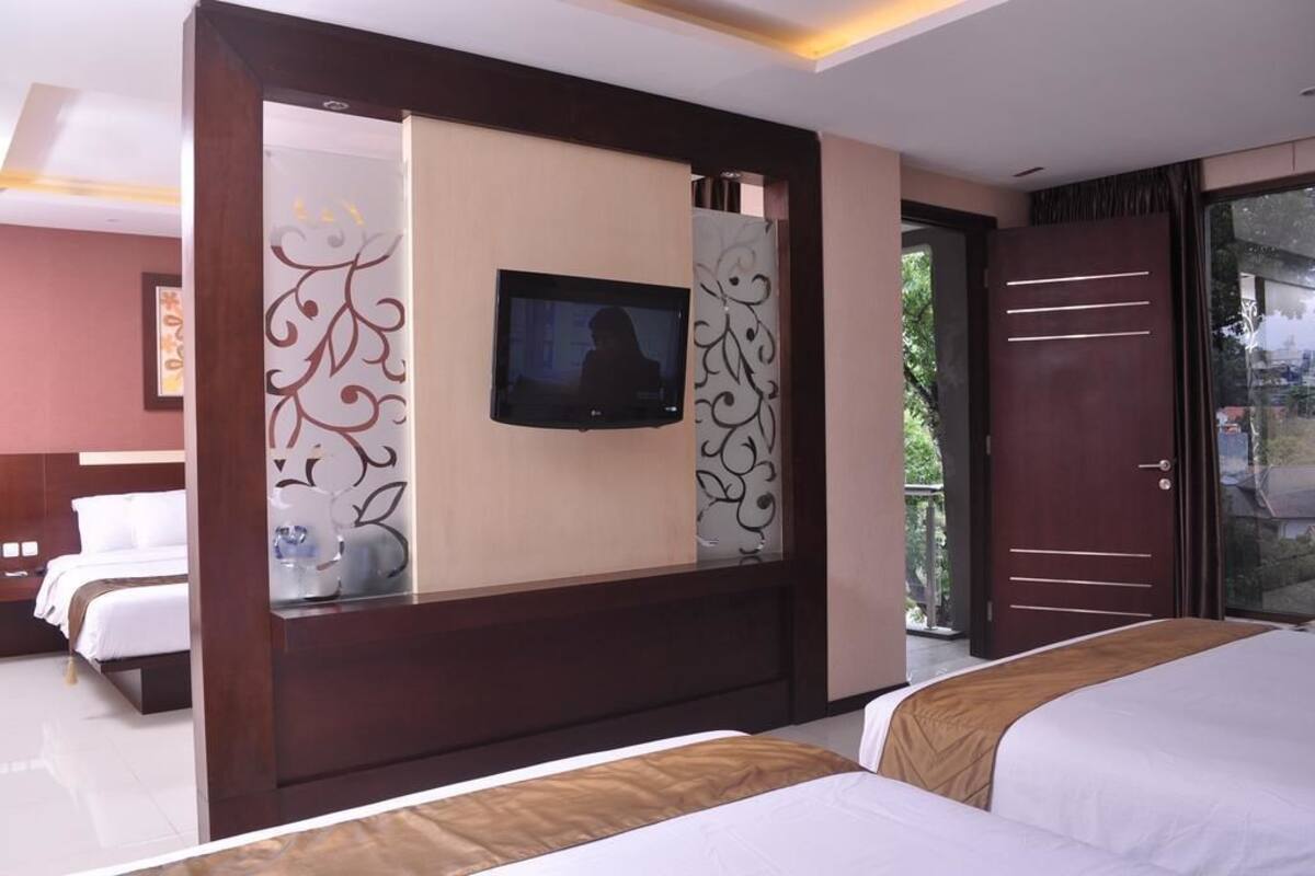 A hotel room with a bed, a TV mounted on a wall, and a sliding door leading to a balcony.