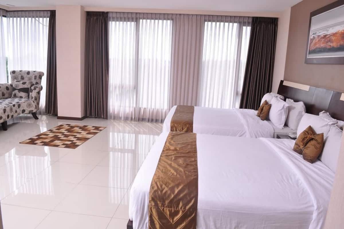 A hotel room with two beds, a chair, and large windows with curtains.