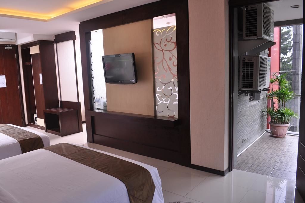 A hotel room with two beds, a TV mounted on a wall, and a balcony with potted plants.