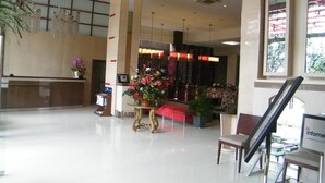 Um hall amplo com uma recepção, uma área de estar com um sofá vermelho e uma mesa grande com flores.