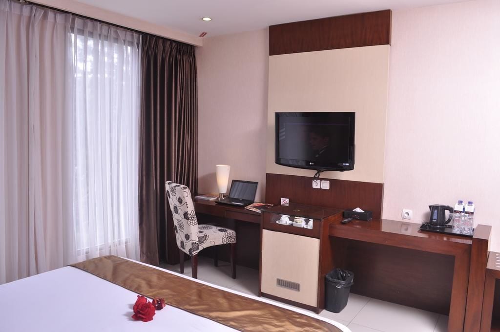 A hotel room with a bed, a desk with a laptop, a television, and a coffee maker.