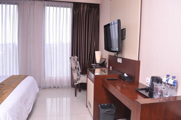 A hotel room with a bed, a desk with a computer, a television, and a window with curtains.