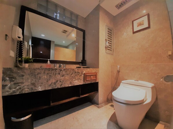 A bathroom with a marble sink, a large mirror, a toilet, and a shower. - The Palais Dago Hotel (Bandung)