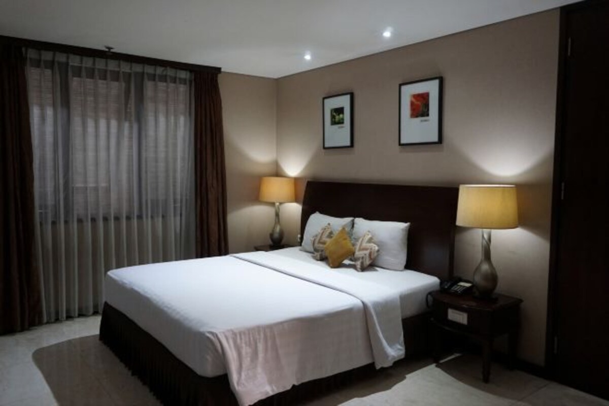 A hotel room with a large bed, two bedside lamps, a nightstand, and two framed pictures on the wall.