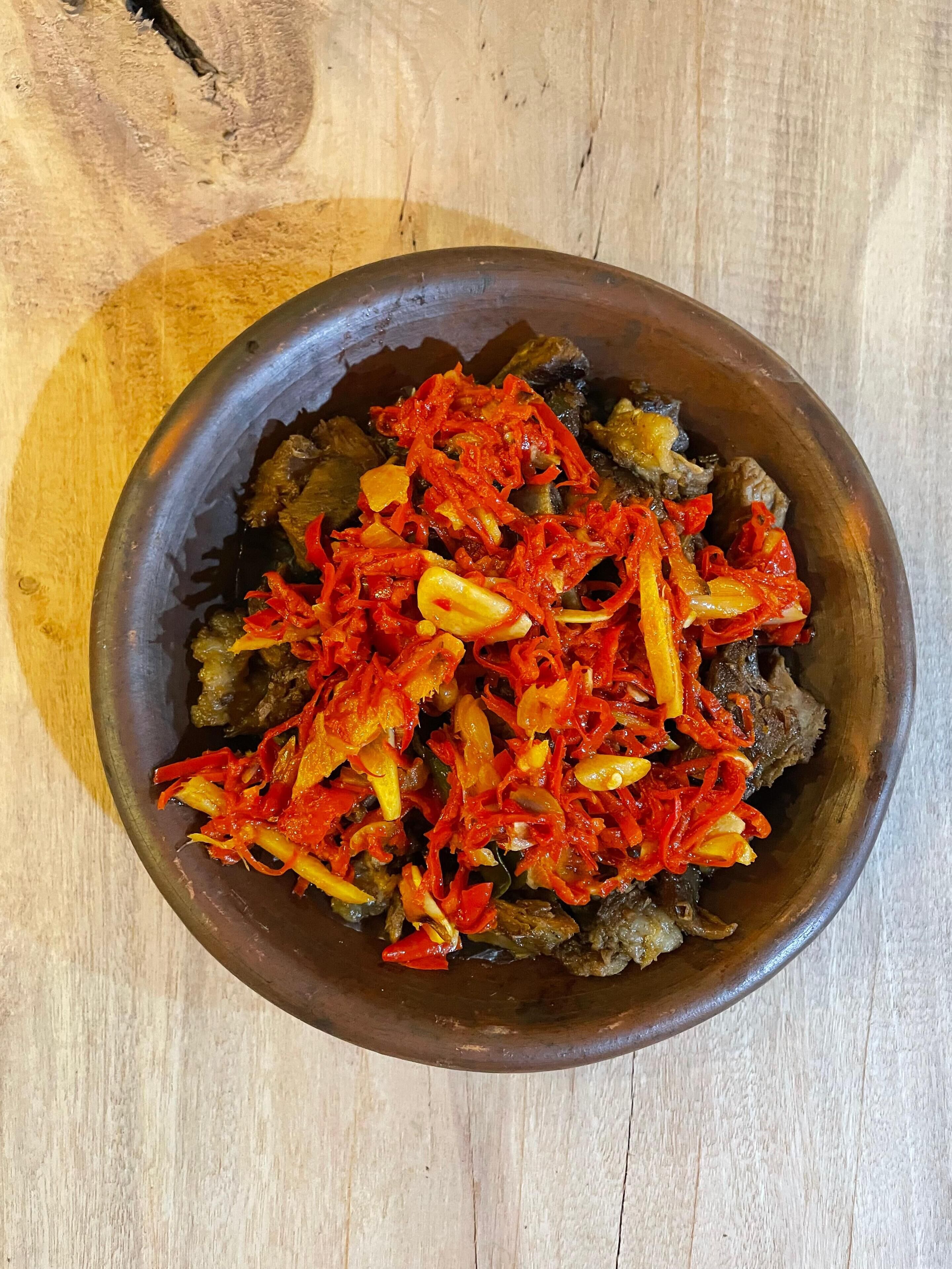 A wooden bowl filled with a dish of meat and red bell peppers.