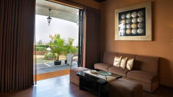 Un salon avec un canapé, une table basse et une vue sur un jardin, visible à travers une porte ouverte.