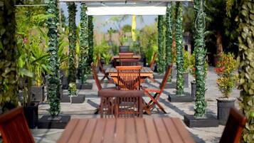 Un espace extérieur aménagé en terrasse, avec des tables et des chaises en bois, entouré de verdure et de plantes en pot.