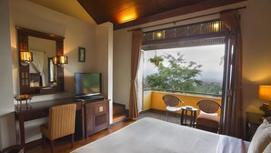 Habitación de hotel con cama, escritorio con televisor, una silla, una mesita y balcón con sillas.