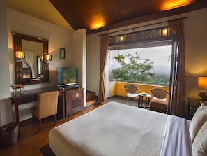Ein Hotelzimmer mit Bett, Schreibtisch mit Fernseher, Stuhl, kleinem Tisch und einem Balkon mit Sitzgelegenheiten.