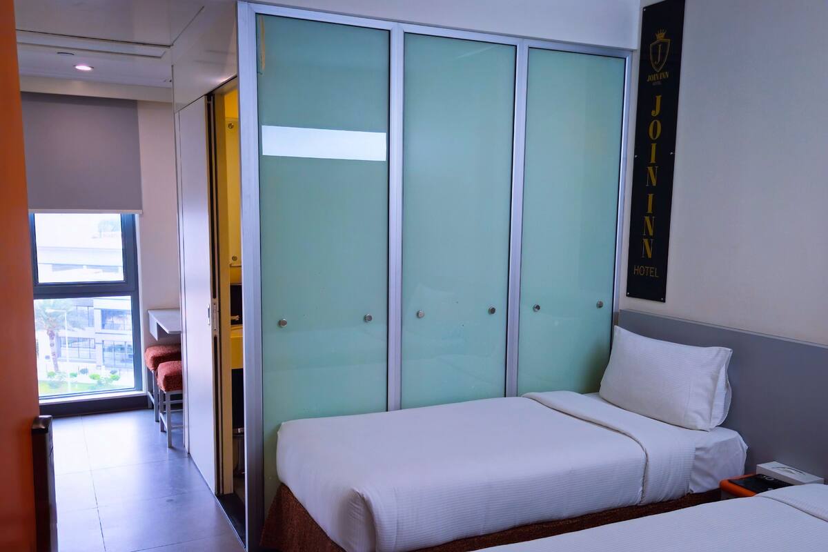 Ein Hotelzimmer mit zwei Betten, einem Schrank mit Milchglas-Türen, einem Bett mit weißem Kopfkissen und einem Schild für das Join Inn Hotel.