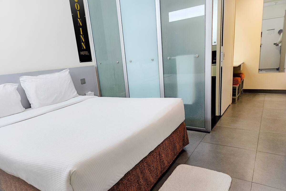 Ein Hotelzimmer mit einem großen Bett, einer Glastür zu einem Badezimmer und einem sichtbaren Schild mit dem Hotelnamen.