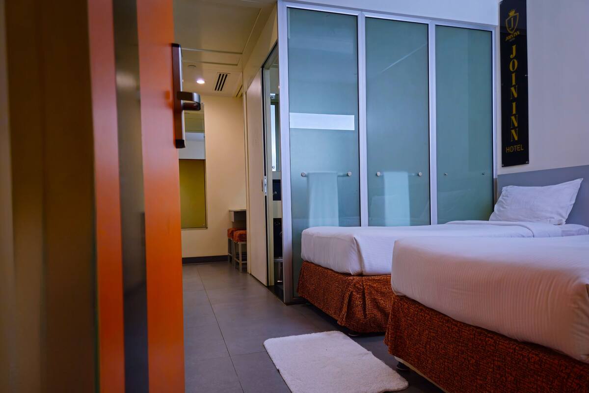 Ein Hotelzimmer mit zwei Betten, einem weißen Teppich und einer Schiebetür, die auf einen Balkon führt.