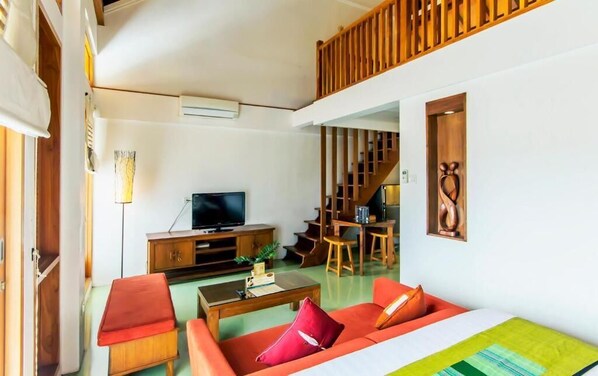 Un espacio habitable compacto con sofá, mesa de centro y televisor. Una escalera conduce a un nivel superior.