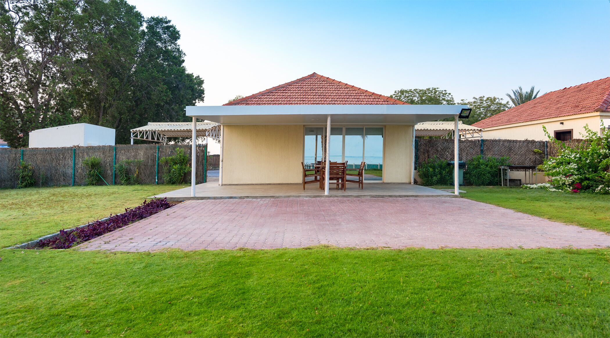 A covered patio area with a table and chairs, surrounded by a well-maintained lawn and a fence.