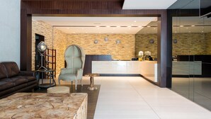 A modern reception area with a stone wall, a reception desk, and a seating area with a sofa and armchair. - Barracuda Beach Resort (Al Rafaah)