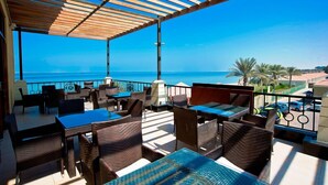 An outdoor terrace with tables and chairs, overlooking a clear blue sea and a distant shoreline. - Barracuda Beach Resort (Al Rafaah)