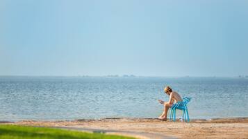 Una persona sentada en una silla azul junto al agua, leyendo un libro.