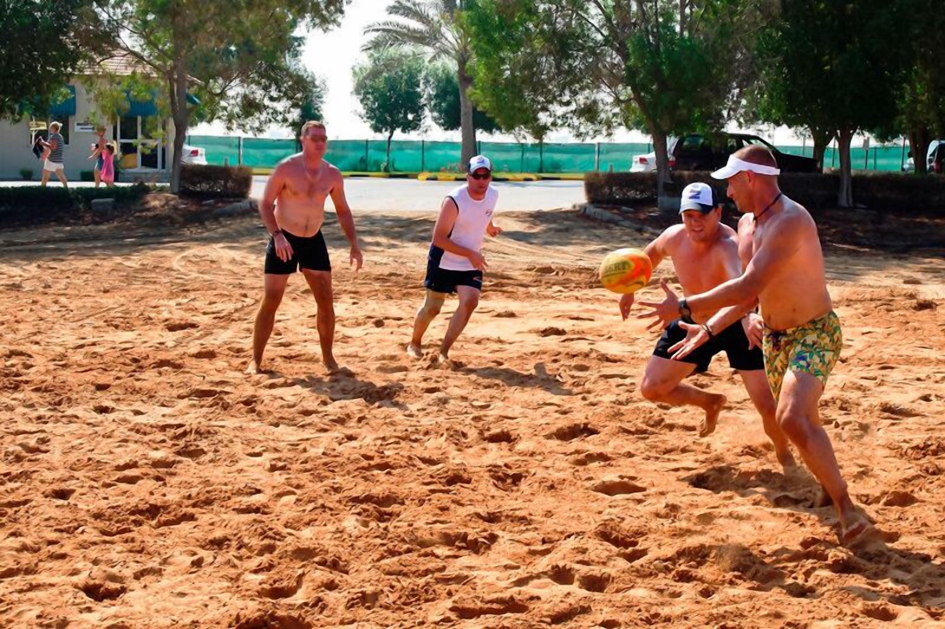A sandy beach with people playing volleyball.
