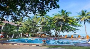 A swimming pool surrounded by palm trees and a building with a tiled roof. - Nuansa Bali (ANYER)