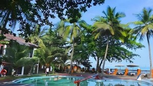 Une piscine entourée de palmiers, un bâtiment avec un toit rouge et un ciel dégagé.
