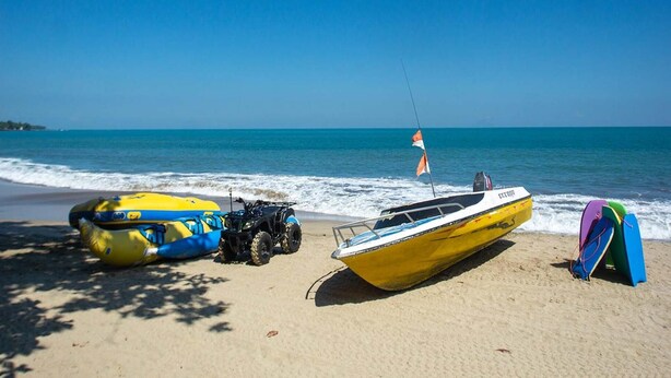 Une plage avec un bateau jaune, un radeau bleu et jaune, et un quad bleu.