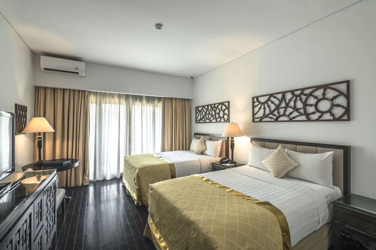 Ein Hotelzimmer mit zwei Betten, einem Schreibtisch, einem Fernseher und einer Klimaanlage.