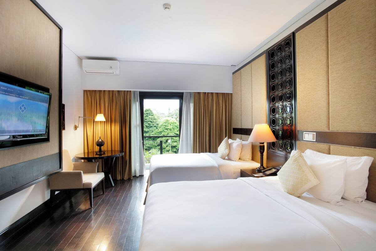 Une chambre d’hôtel avec deux lits, une télévision, un bureau et une fenêtre avec des rideaux.