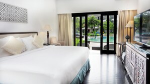 Habitación de hotel con una cama grande, un escritorio con televisor y vistas a una piscina y zonas verdes.