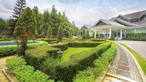 Un jardín bien cuidado con setos ordenados, diversas especies de árboles y un edificio de estilo arquitectónico moderno.