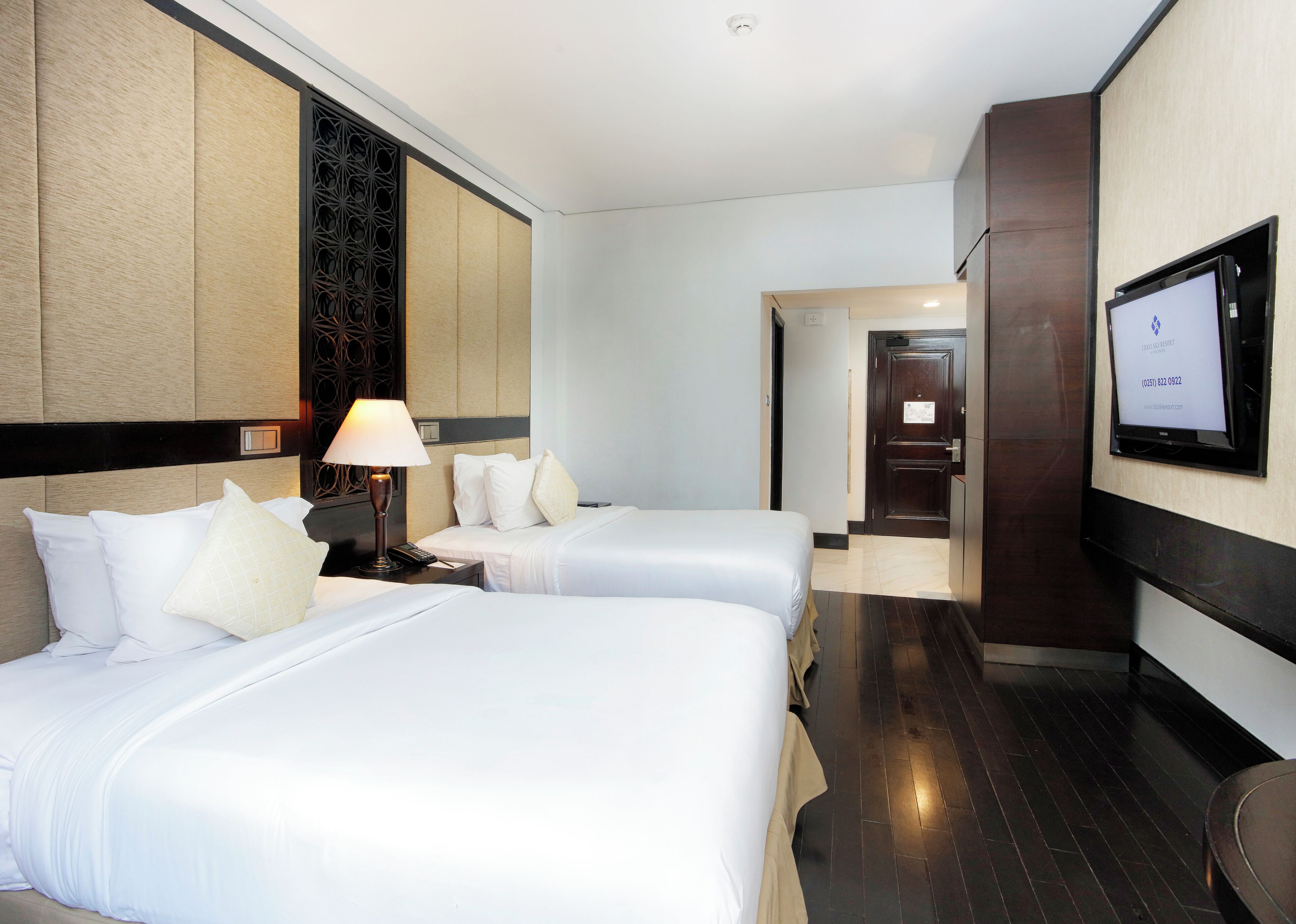 A hotel room with two beds, a TV mounted on the wall, and a door leading to another room.