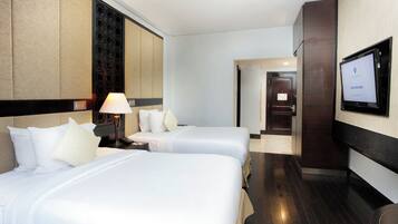 A hotel room with two beds, a TV mounted on the wall, and a door leading to another room.