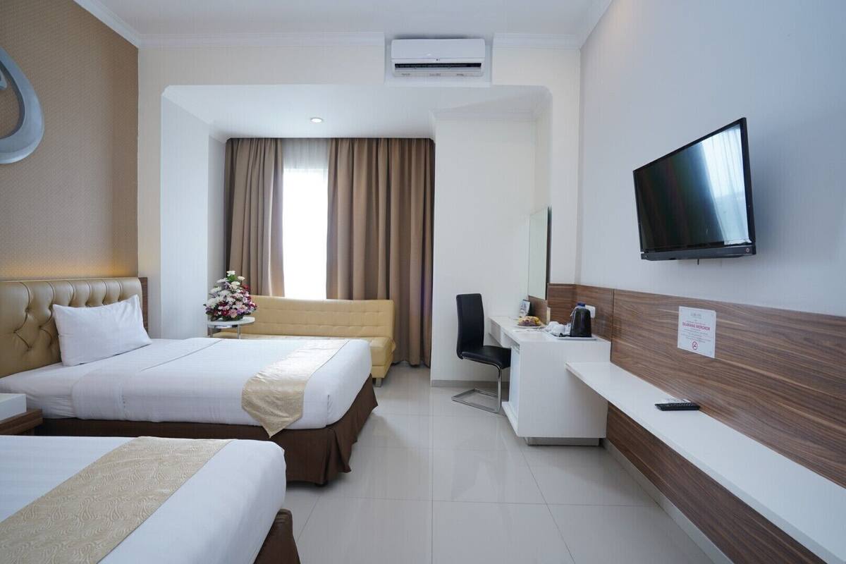 Habitación de hotel con dos camas, un escritorio, una silla, un televisor y aire acondicionado.