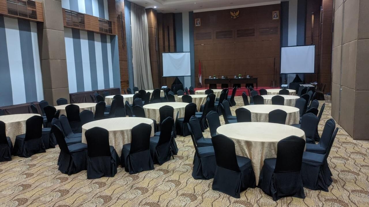 A conference room with round tables and chairs, a podium, and a projection screen.