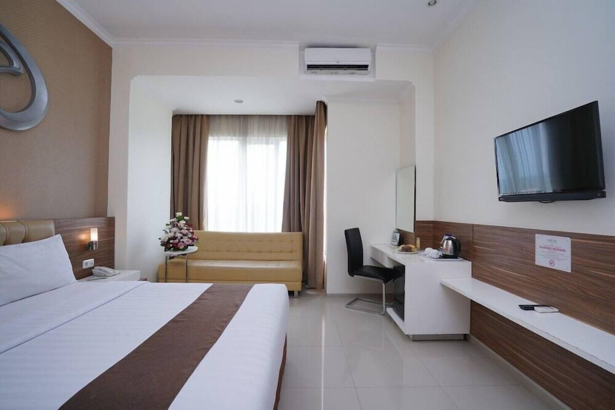 Habitación de hotel con cama, escritorio, silla, televisor y ventana con cortinas.