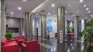 A modern lobby with red seating, large metallic pillars, and a reception area with a cityscape poster. - Lorin Sentul Hotel (Bogor)