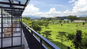 A balcony with a glass enclosure, outdoor seating, and a view of a green landscape with trees and a distant building. - Lorin Sentul Hotel (Bogor)