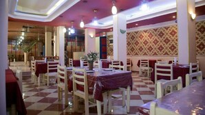 A restaurant with checkered flooring, red tablecloths, and white chairs. - Pharaohs Hotel (Luxor)