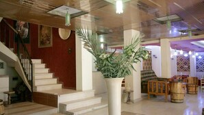 A spacious lobby with a grand staircase, a large white vase with greenery, and wooden barrels. - Pharaohs Hotel (Luxor)