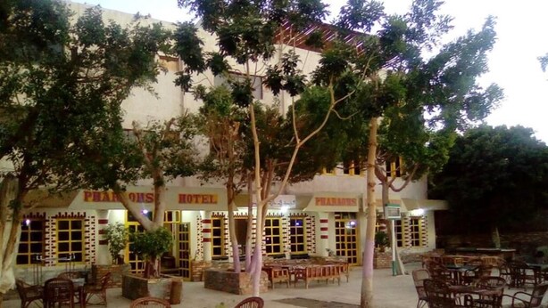 An outdoor seating area with wicker furniture, a building with multiple rooms labeled 'Pharaohs Hotel', and trees providing shade. - Pharaohs Hotel (Luxor)