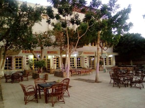 An outdoor seating area with wicker furniture, a building with multiple rooms labeled 'Pharaohs Hotel', and trees providing shade. - Pharaohs Hotel (Luxor)