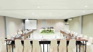 Ein Konferenzraum mit langem Tisch, mehreren Stühlen und einer Präsentationsleinwand.
