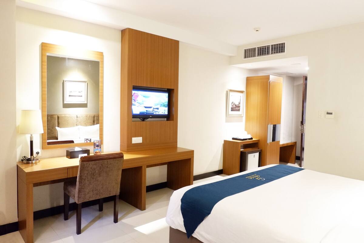 Habitación de hotel con cama, escritorio, silla, televisión y espejo.