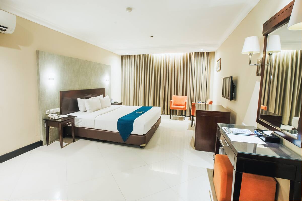 Una habitación de hotel con cama, escritorio, silla, espejo y cortinas.